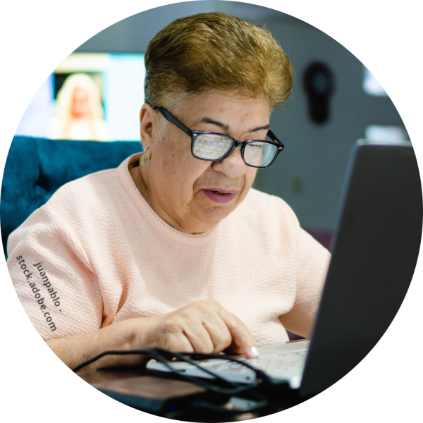 Eine ältere Frau mit Brille tippt etwas in einen Laptop.