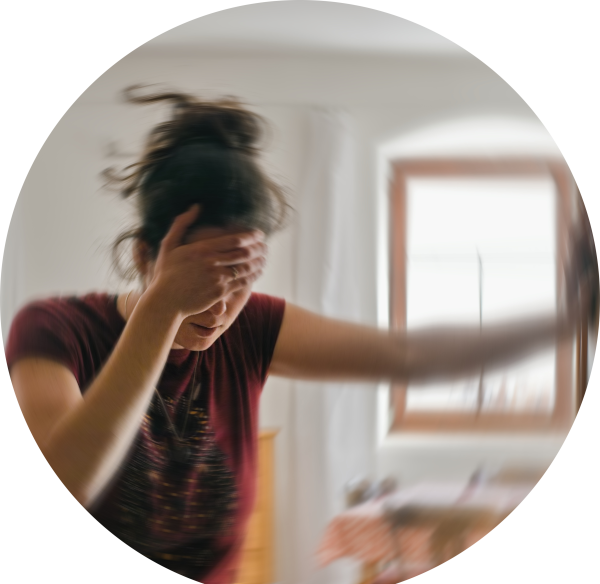 Eine Frau hält sich den Kopf und stützt sich am Türrahmen ab; verwaschener Hintergrund.